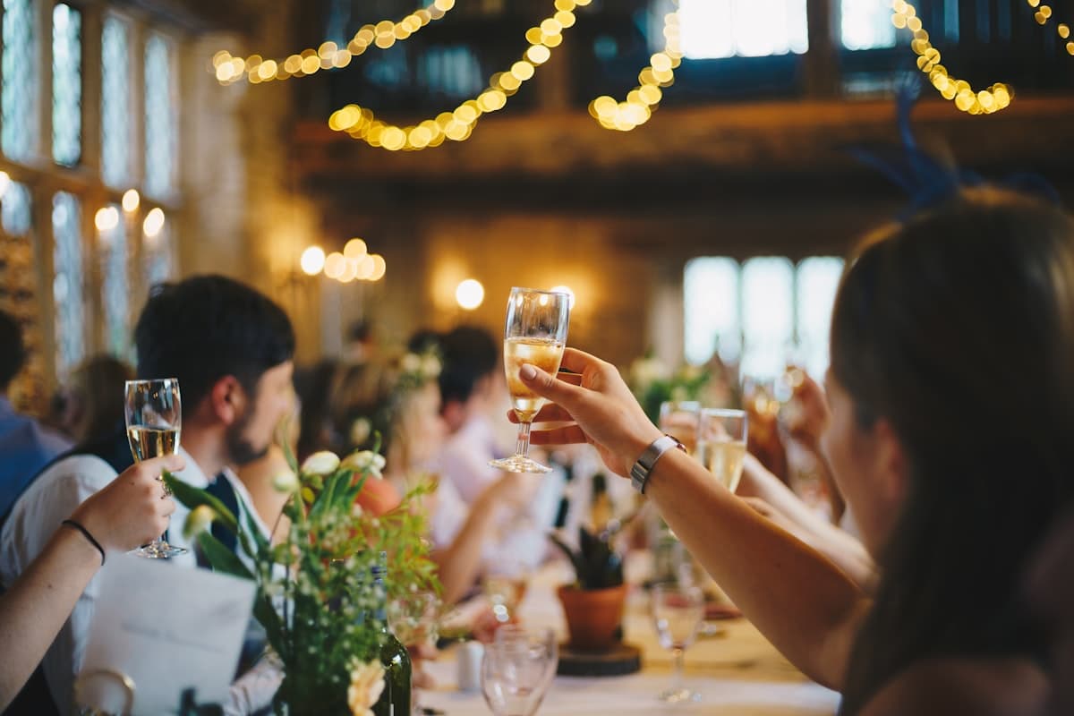 Elegantly dressed guests raising glasses of wine in celebration at a dinner table.